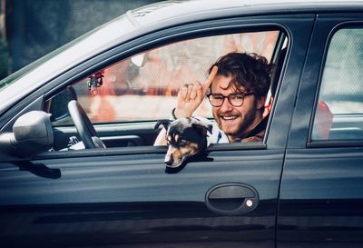 Portrait of smiling young man with dog sitting in car