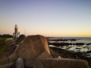 Lighthouse by sea against clear sky during sunset