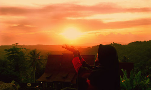Man holding orange against sky during sunset