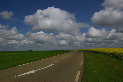 Empty road amidst field against sky