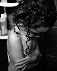 Side view of naked girl with curly hair standing with arms crossed