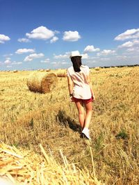 Rear view of woman walking on grassy field against sky during sunny day