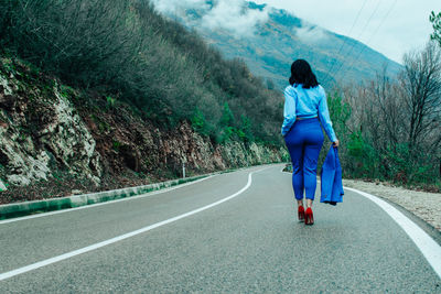 Rear view of woman walking on road by mountain