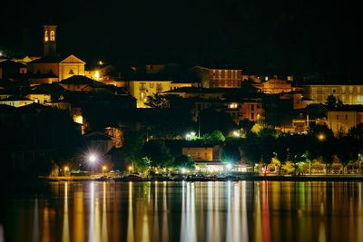 Illuminated city by river against sky at night