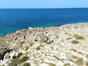 High angle view of man walking on rocks by ocean