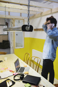 Side view of young man answering smart phone in creative office