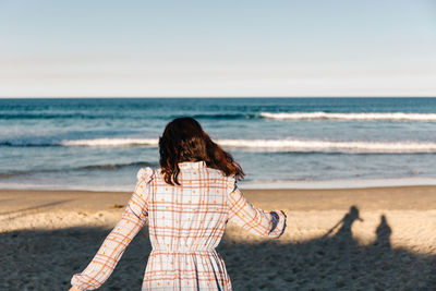 Rear view of woman standing at beach against sky