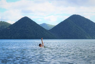 Boy swimming in sea against mountains