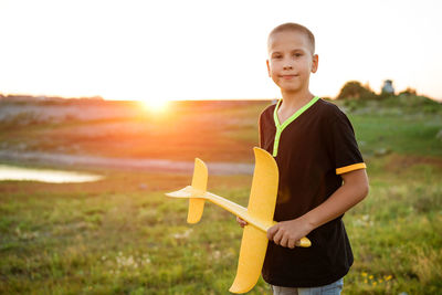 Boy throws a toy airplane in the summer at sunset.