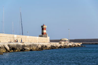 Lighthouse by sea against clear sky