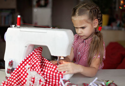 Cute girl using sewing machine at home