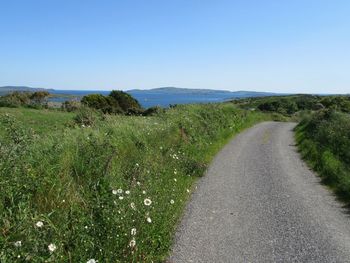 Road passing through field against clear sky