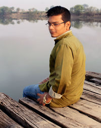 Young man sitting on pier over lake