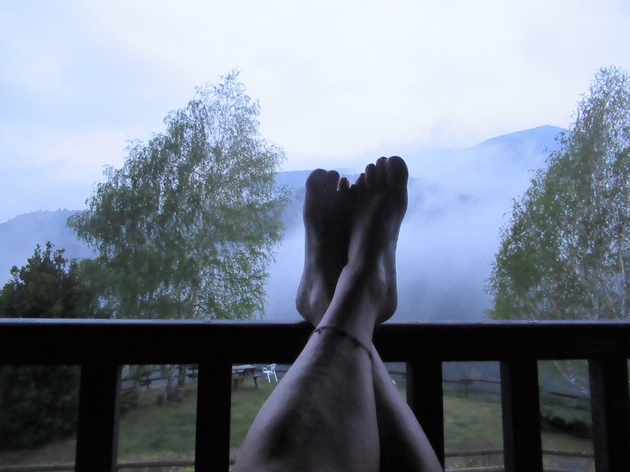 railing, tree, sky, nature, one person, human leg, limb, low section, relaxation, plant, leisure activity, lifestyles, day, adult, human limb, human foot, cloud, mountain, tranquility, outdoors, barefoot, morning, women, personal perspective, vacation, beauty in nature, tranquil scene, blue, scenics - nature, water, feet up, architecture