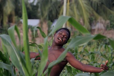 Portrait of shirtless man with arms outstretched by plants