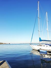 Sailboats moored in sea against clear blue sky