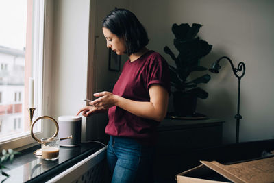 Woman holding smart phone while using equipment by window