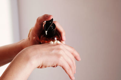 Hands of a young woman gently squeezing cream from a container to moisturize dry skin