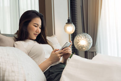 Young woman using mobile phone on bed at home