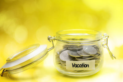 Close-up of coins in jar on yellow background