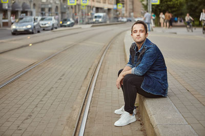 Portrait of young man sitting on footpath in city