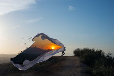 Sunset with birds on fabric held by man on field against sky