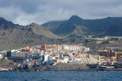 Town by sea and mountains against sky