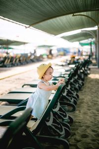 Girl sitting on lounge chair at beach against sky