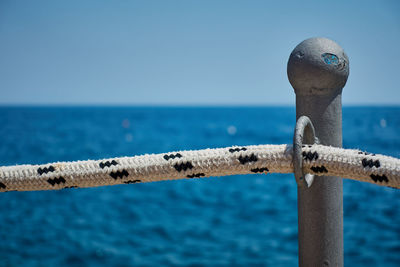 Close-up of metal against sea against clear blue sky