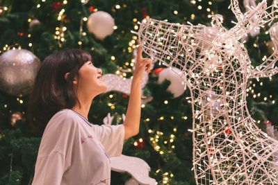 Side view of smiling girl looking at illuminated christmas decoration at home