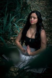High angle view of woman with eyes closed mediating on land in forest
