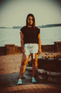 Portrait of young woman standing at sea shore against sky