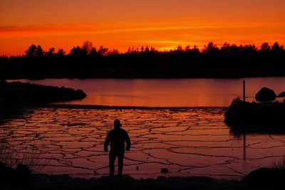 Silhouette man standing by lake against sky during sunset