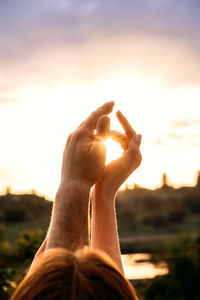 Close-up of hand against sunset sky