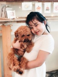 Portrait of girl carrying brown poodle at home