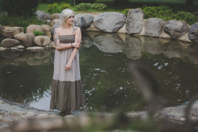 Full length of young woman in dress standing by pond