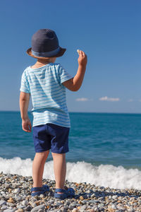 A child in blue hat on the sea coast looks out at the sea