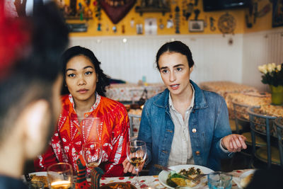 Young women talking with male friend during dinner party at restaurant