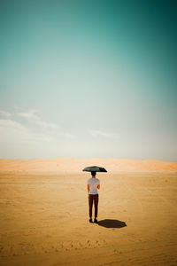 Rear view of man standing in desert with umbrella