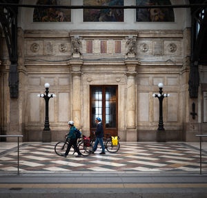 People riding bicycle on street against building