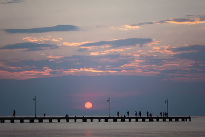 Silhouette people by sea against sky during sunset