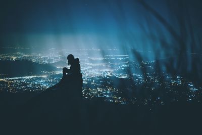 Silhouette of person against illuminated cityscape at night