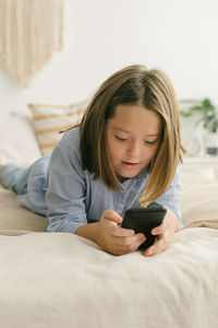 Young woman using mobile phone while lying on bed at home