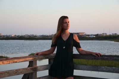 Young woman standing on pier over river at sunset