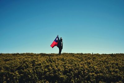 Person paragliding on field against clear blue sky