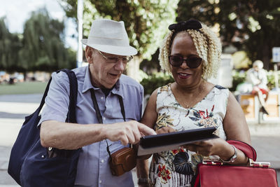 Smiling senior couple using digital tablet on street during sunny day