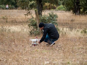 Side view of man crouching by drone on grass