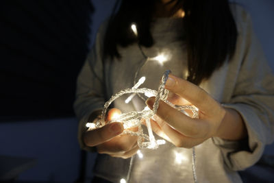 Close-up midsection of woman holding illuminated string lights