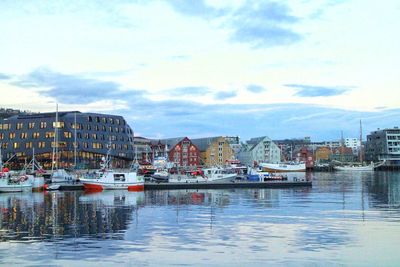 Boats moored at harbor against sky in city