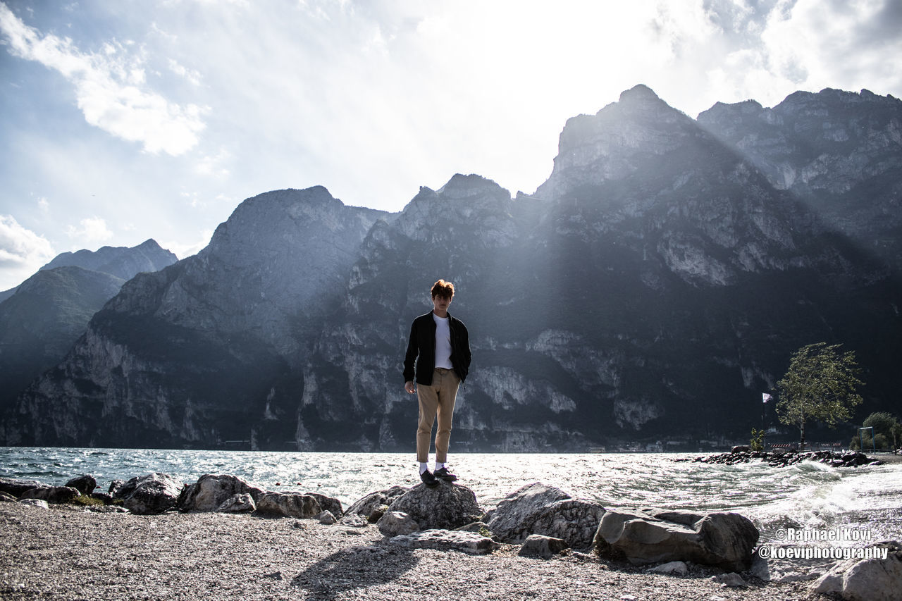 mountain, one person, beauty in nature, scenics - nature, full length, real people, sky, rock, leisure activity, rock - object, solid, lifestyles, water, non-urban scene, standing, nature, young adult, tranquil scene, mountain range, outdoors